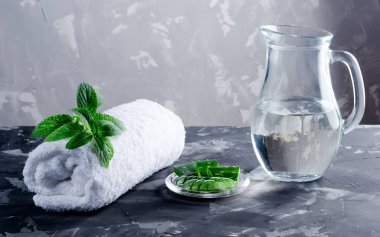 Beyaz havlu, nane, aloe ve koyu beton bir masada bir sürahi su..