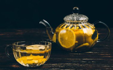 Cam çaydanlık ve bir bardak limonlu çay ve ahşap bir masada otlar..