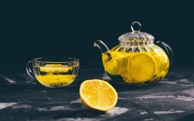 Ahşap bir masada şeffaf çaydanlık ve limonlu bardak.