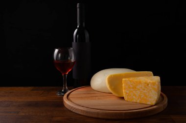 Set of cheeses and red wine on a wooden stand on a black background.