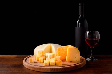 Yuvarlak bir ahşap tezgahta farklı çeşitteki peynirden dilimler, bir şişe ve bir bardak şarap eski bir masanın üzerinde..