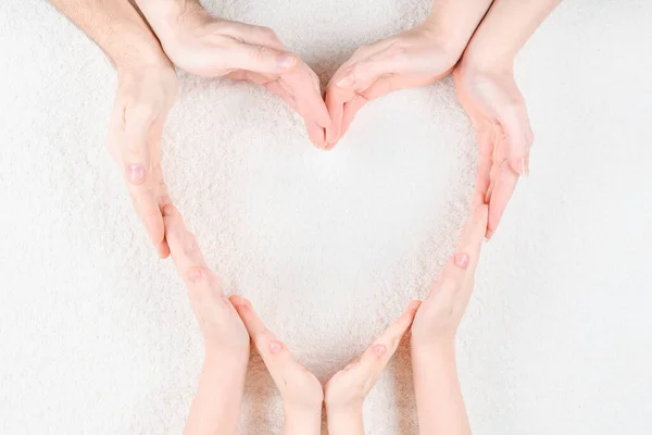 Heart from the hands of parents and children on a white soft fabric. The concept of a large loving family or a symbol of the international family day. Close-up view from above.
