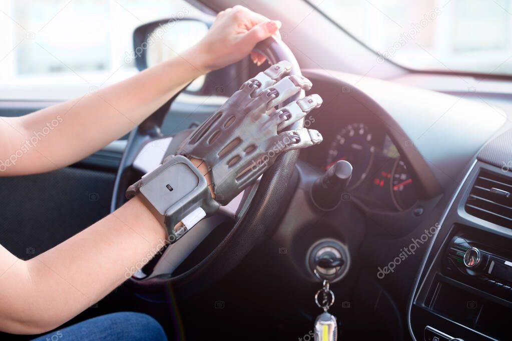 A girl with a prosthetic arm drives a car. The concept of a full life for people with disabilities. Side view, small depth of field.