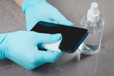 Disinfection of the phone using antiseptic agents by a person wearing gloves. The concept of disinfection of gadgets that could be touched by infected people in the conditions of an epidemic and quarantine. clipart