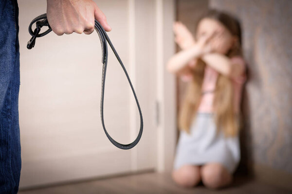 Мужчина с ремнем в руке угрожает маленькой девочке. Маленькая девочка стоит на коленях в углу и защищает себя, скрестив руки перед лицом. Концепция домашнего насилия в отношении ребенка
.