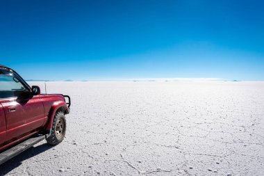 44 'lük bir sürüş turu uçsuz bucaksız, desenli Uyuni tuzlu arazisinde açık mavi gökyüzü günündeki uzak dağlara doğru yol alır..