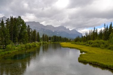 Yüzeyinde hafif yağmur damlaları olan Bow River 'ın berrak suları. Kanada 'daki bu soğuk ve nemli günde bulutlar kayalık dağ sırasının tepesinde kayarak ilerler..