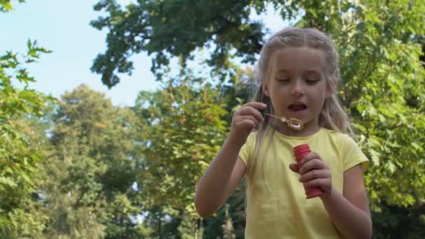 Милая кавказская девушка, пускающая мыльные пузыри в парке, ребенок веселится на открытом воздухе — стоковое видео