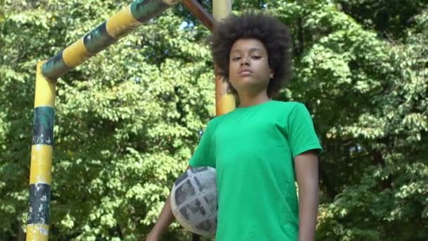 Black male teenager looking camera holding football, sport training outdoor — Stock Video