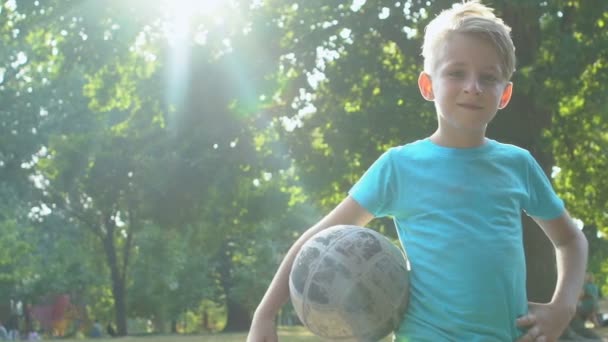 Smiling male kid holding football outdoors on summer sunny day, healthy activity — Stock Video