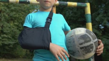 Top tutarken kolu yaralanmış aktif bir çocuk. Kamera görünümlü, spor sakatlığı var.