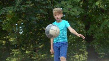 Aktif çocuk eski futbol topunu tekmeliyor, iyileşme kaydediyor, sokak futbolu eğitimi alıyor.