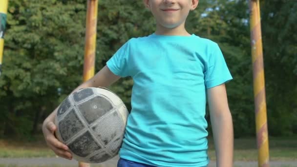 Niño varón feliz sosteniendo el fútbol de pie en la puerta del campo, club deportivo, competencia — Vídeos de Stock