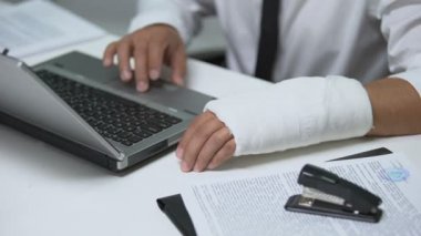 Alçıtaşında kolu kırık bir iş adamı laptopta, travmada, işkoliklerde daktilo yazıyor.