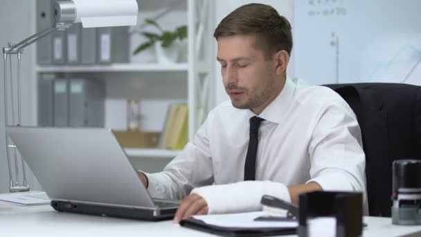 Hombre adicto al trabajo con el brazo roto en yeso escribiendo una mano en el ordenador portátil PC, trauma — Vídeos de Stock