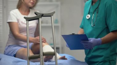 Doktor, bacak travması ve ortopedik ekipmanlı bir kadına rehabilitasyon planından bahsediyor.
