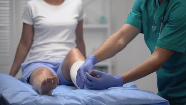 Ортопед фиксирует эластичное искривление на ноге пациента после спортивной травмы, здравоохранения — стоковое видео