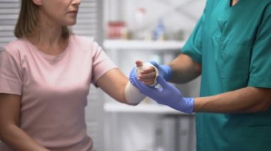 Kadın hasta koluna elastik sargı yapan doktor, travma sonrası rehabilitasyon.