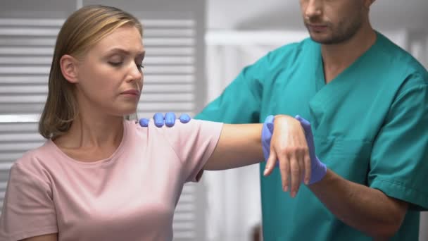 Cirurgião examinando triste paciente ombro após trauma, levantando a mão feminina, reabilitação — Vídeo de Stock