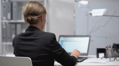 Uyuşmuş boynuna masaj yapan yorgun bir kadın laptopta çalışıyor, sinirleri gerilmiş, arkadan bakıyor.