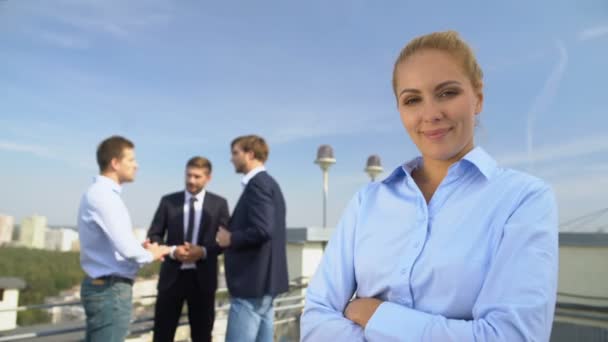 Successful lady boss smiling on camera outdoors, male colleagues background — Stock Video