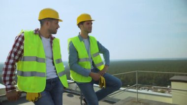 İki inşaat işçisi iş molası sırasında çatı ve işgalde konuşuyor.