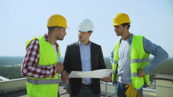 Молодий чоловічий бос в шоломі безпеки обговорює план будівництва з робітниками — стокове відео