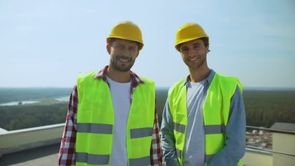 Trabalhadores da construção profissional em capacetes de segurança e jaquetas sorrindo câmera — Vídeo de Stock