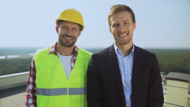 Travailleur de la construction en casque et réalisateur souriant à la caméra, équipe professionnelle — Video
