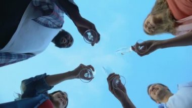 Şampanya kadehlerini tokuşturup kutlama yapan çok ırklı arkadaşların taban görüntüsü.