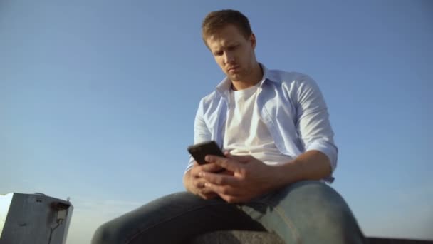 Hombre deprimido con teléfono inteligente sentado en el borde del techo después de la ruptura de la novia — Vídeos de Stock
