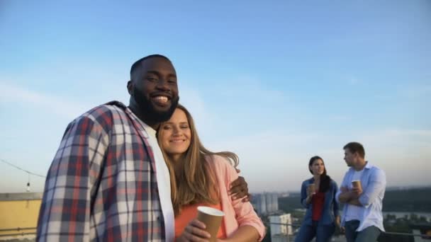 Multiethnic couple hugging and looking at camera, spending time at roof party — ストック動画