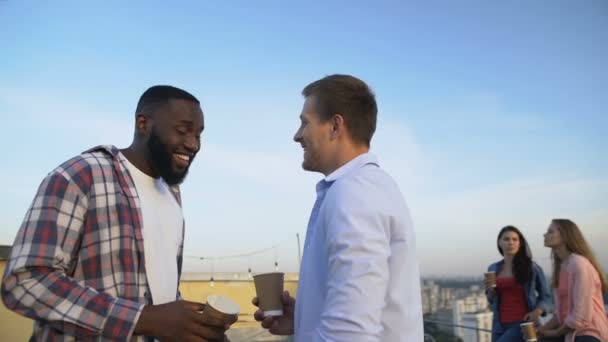 Багатоетнічні друзі чоловічої статі розмовляють і сміються на вечірці на даху, розслабляючись разом — стокове відео