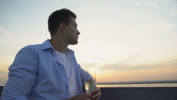 Nachdenklicher junger Mann mit einem Glas Champagner und Blick von der Terrasse auf den Sonnenuntergang — Stockvideo