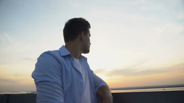 Красивий молодий чоловік дивиться захід сонця з тераси, думає про життя, проблеми — стокове відео