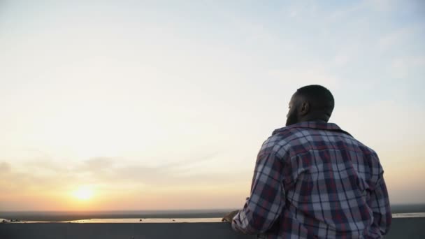 Vista trasera del hombre afroamericano disfrutando de la puesta de sol desde la azotea, soñando de día — Vídeos de Stock