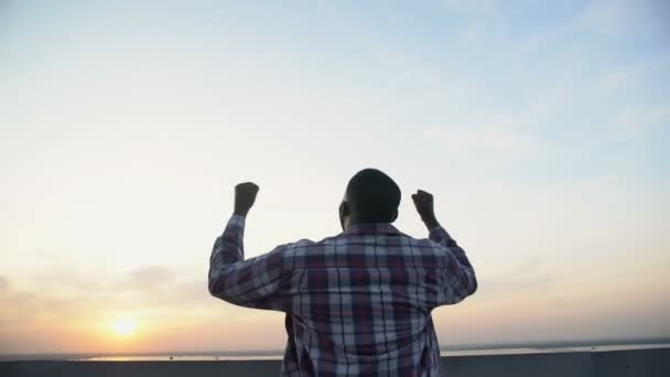 Visão traseira do homem negro levantando as mãos para o céu contra o pôr do sol, realização, vencedor — Vídeo de Stock