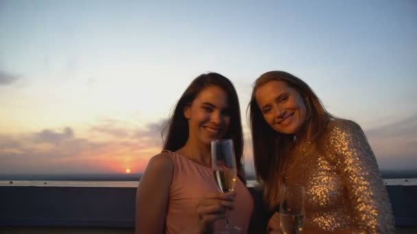 Glada kvinnor med glas champagne poserar vid kameran på terrassen vid solnedgången — Stockvideo