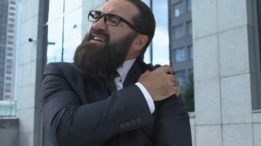 Üzgün iş adamı iltihaplı omzunu ovuyor, artrit ağrısı çekiyor, ağır çekimde.