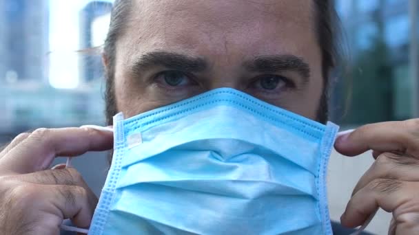 Hombre serio poniendo en primer plano mascarilla médica, gran ciudad concepto de contaminación del aire — Vídeo de stock
