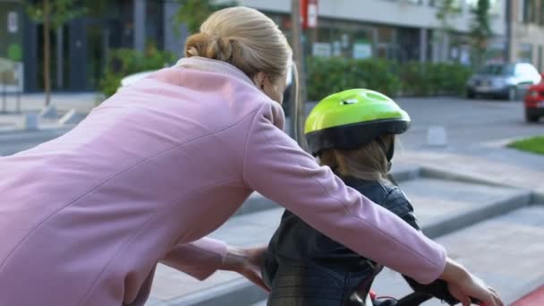 Sevgi dolu bir anne kızına dışarıda bisiklet sürmeyi öğrenmesi için yardım ediyor. — Stok video