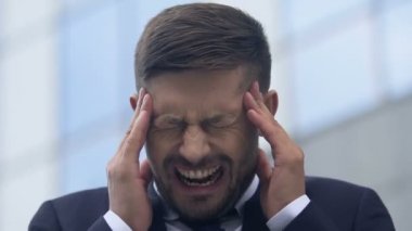 Şakaklardaki keskin acıdan, stresli hayattan ve iş yerindeki stresten dolayı yüzünü buruşturan hasta bir adam.