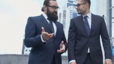 Mutlu iş ortakları dışarıda yürüyor, dostça sohbet ediyor, gülümsüyor.