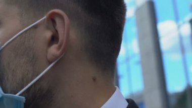 Yüzü maskeli ciddi bir adam kameraya bakıyor, şehirdeki hava kirliliğinden endişe ediyor.