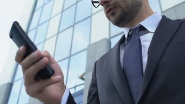 Sinirli iş adamı dışarıda akıllı telefondan mesaj atıyor. Mesajı okuduktan sonra gergin.