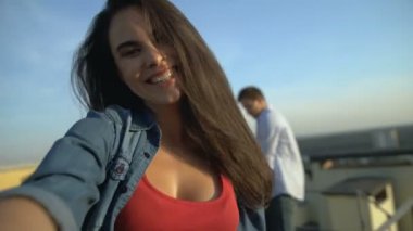 Esmer kız çatıdaki partide video kaydediyormuş, arkadaşlar arka planda dans ediyormuş.