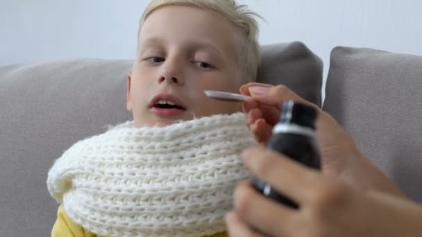 Заботливая мама дает сироп от кашля больной мальчик носит шарф, лечение боли в горле — стоковое видео