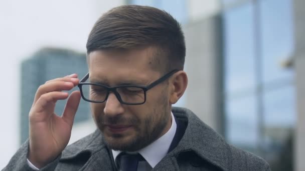 Молодой человек снимает очки и массирует виски, страдая от высокого давления — стоковое видео