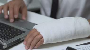 Bilek travması geçiren bir ofis müdürü dizüstü bilgisayarda çalışıyor, çalışan hakları koruması var.