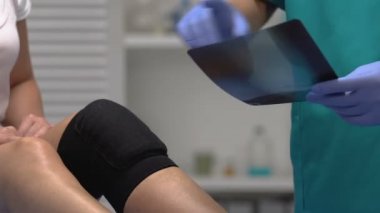 Doktor, dizlik ve travma geçiren hastaya röntgen sonuçlarını açıklıyor.